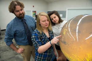 STEM Resource Center Manager Colin Wilson looks on as SIUE students Valerie Becker and Emily Chappel examine a high-resolution image of the surface of Mars. 