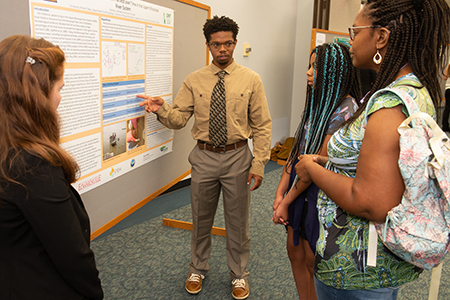 REU participant Anthony DeFreece, a sophomore studying anthropology at the University of North Texas, explains his research project to his sister Sophia and mother Valerie as his research partner Caille Paulsen looks on.