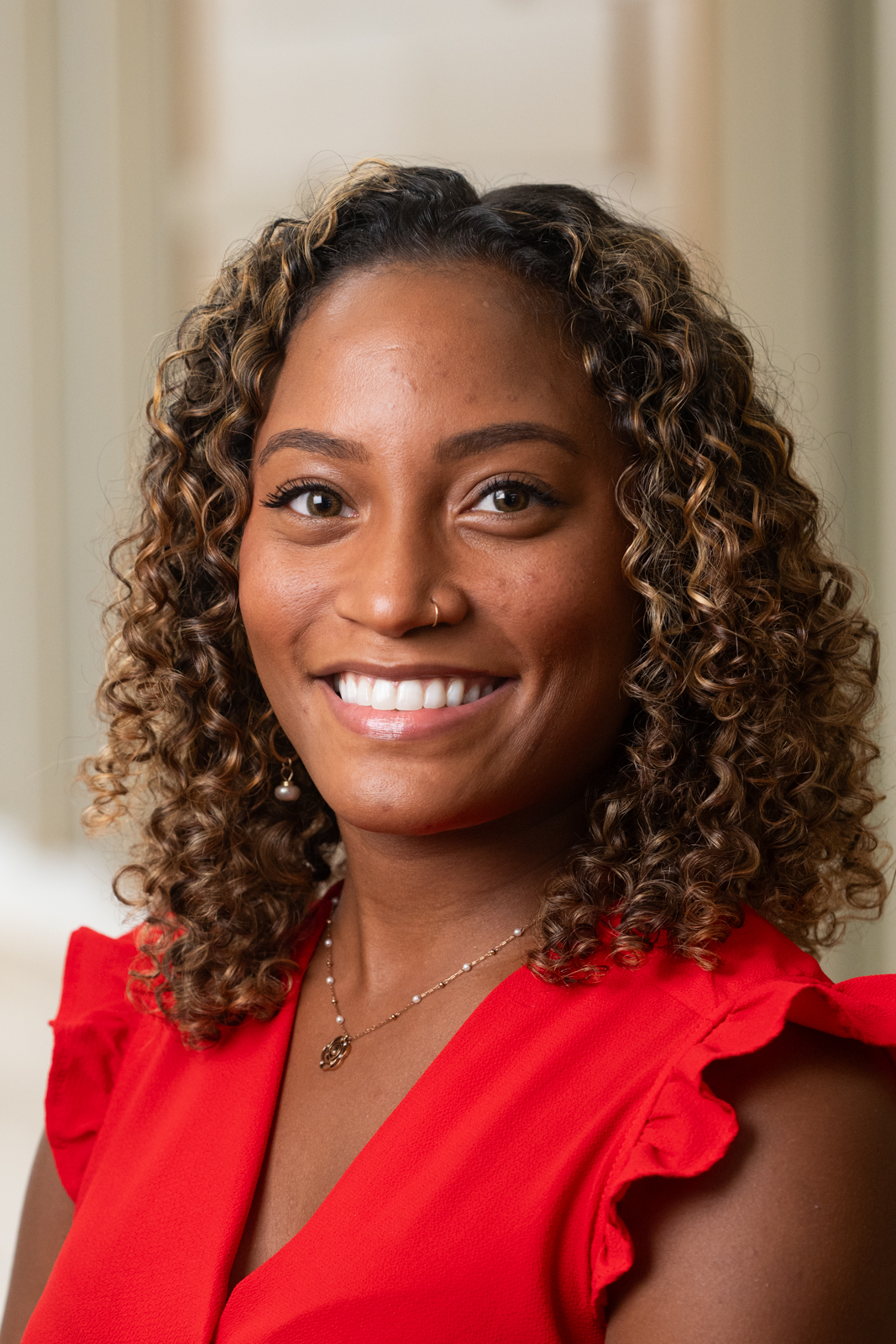 A portrait of Taylor Cross, an African-American woman with curly hair wearing a red blouse. Taylor has a warm, welcoming smile.