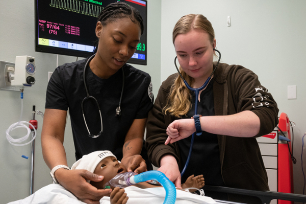 Two nursing students practice care on infant doll