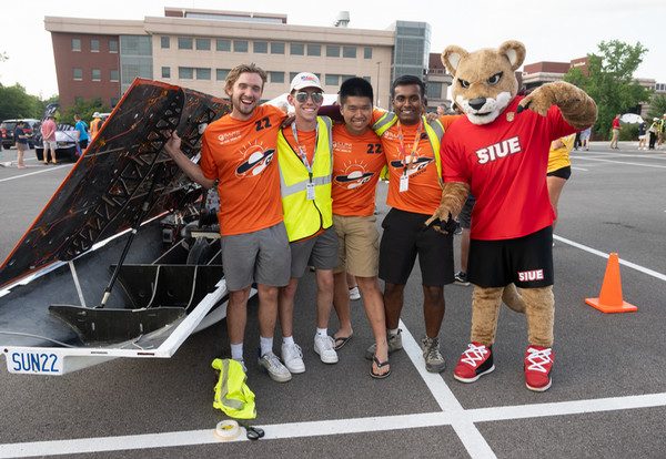 A solar car driving team stands in front of solar car and pose for photo with Eddie the Cougar mascot