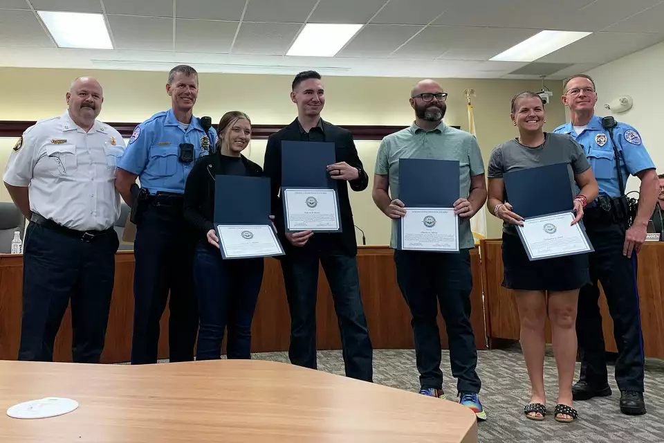 Edwardsville Fire Chief James Whiteford, Edwardsville Police Chief Michael Fillback, Lyndsey Holder, Dakota Moore, Charles Silvey, Samantha Smith and Edwardsville Police Lt. Brandon Whittaker. They are being photographed at a City Council Meeting. They are holding awards, which look similar to a dikoma cover.