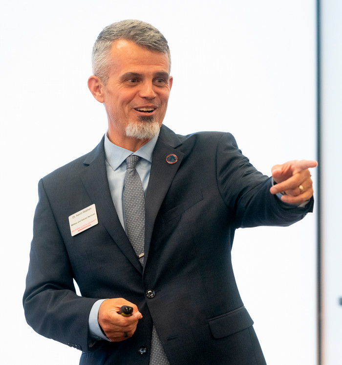 Photo of Kevin Wathen speaking in front of a daylit window. He is smiling and open handed with enthusiasm