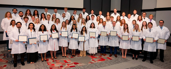 Class of 2028 stand on risers holding their signed pledge and oath as first year dental students