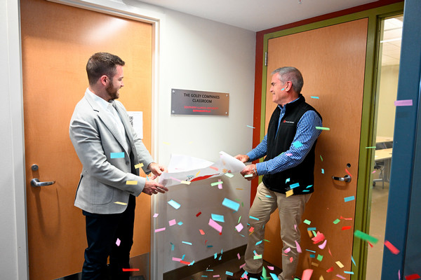 Confetti flies in front of father son who unveil room dedication sign outside classroom door