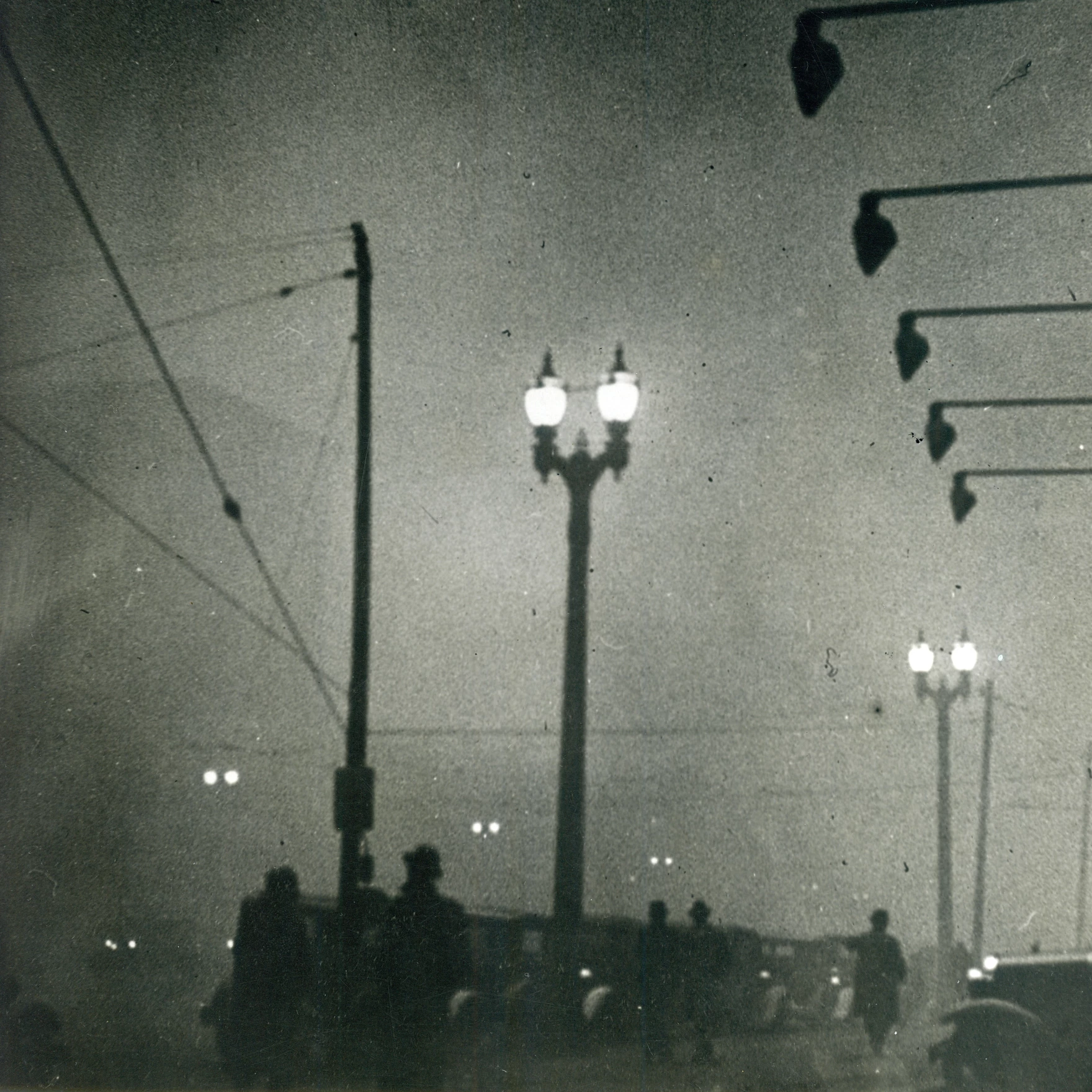 Black-and-white photograph showing silhouetted figures standing beneath streetlights in heavy pollution at night along a St. Louis city street.