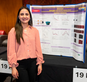 A student stands beside a research poster displayed on an easel during an academic poster presentation.